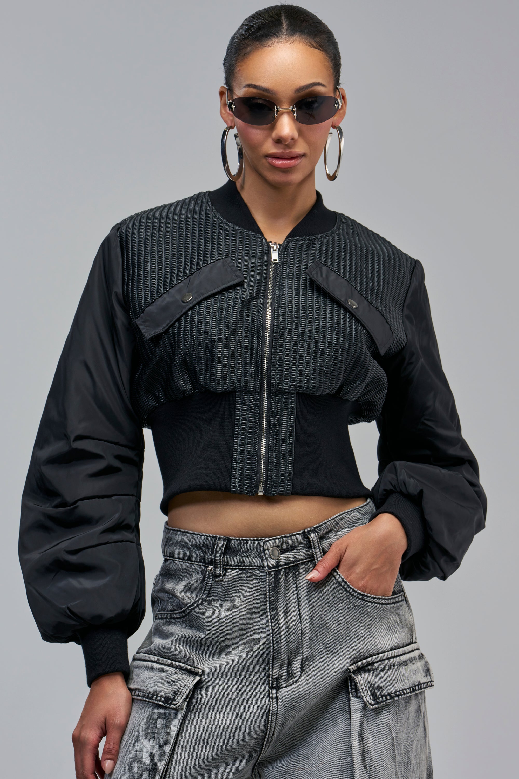 A person wearing a SHAY MIXED MEDIA BOMBER, a cropped black jacket with textured paneling and voluminous sleeves.