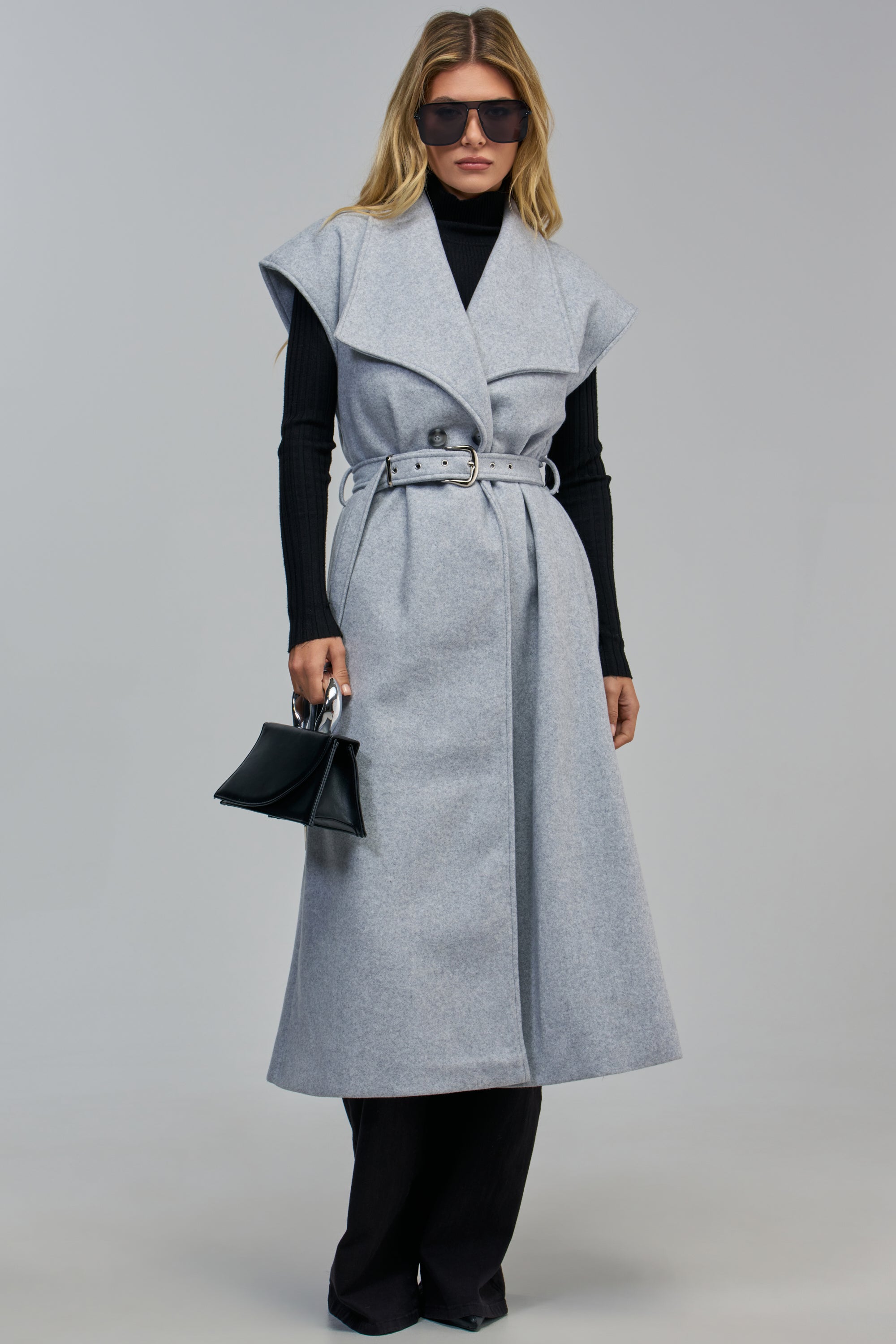 A woman wearing a grey SIMONE FAUX WOOL VEST over a black long-sleeved shirt and trousers, holding a small black handbag.