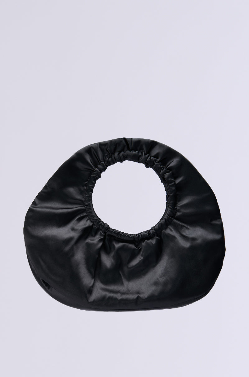 The FANNED OUT SATIN PURSE is a chic oversized handbag featuring a circular handle, a smooth and slightly shiny texture, and an elegant gathered design around the handle opening. Its minimalist style is accentuated against a solid light gray background.