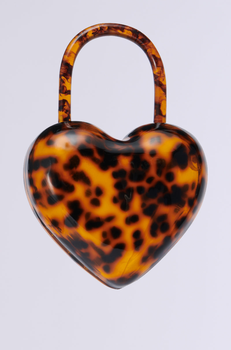The HEART ON LOCK PURSE, showcasing a chic tortoiseshell pattern and matching handle, is set beautifully against a plain white background. Its look is perfected with a stylish acrylic base, adding an element of modern elegance.