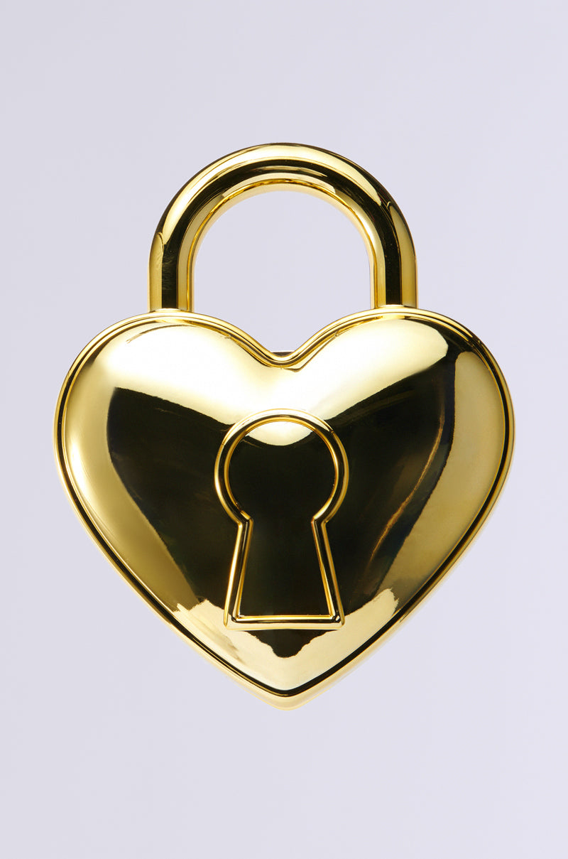 The HEART ON LOCK PURSE features a gold, heart-shaped padlock adorned with rhinestone embellishments and a central keyhole, set against a plain gray background.