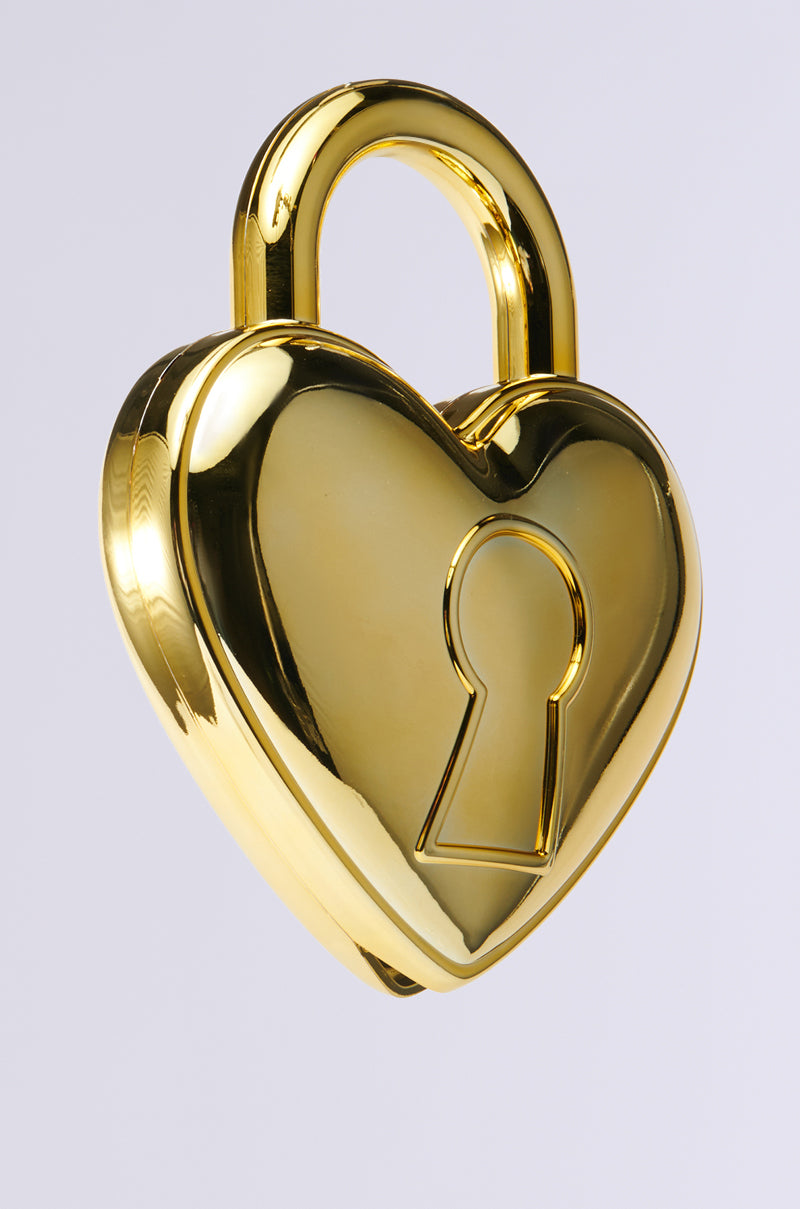 The HEART ON LOCK PURSE is a shiny gold padlock in a heart shape with rhinestone accents around the center keyhole, set against a plain gray background.