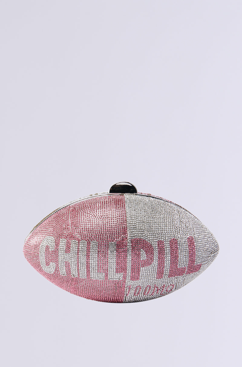 Introducing the "TAKE A CHILL PILL CLUTCH," a capsule-shaped handbag featuring rhinestone embellishments, pink and silver colors with "CHILL PILL" text, complemented by a metallic chain link strap and clasp closure.