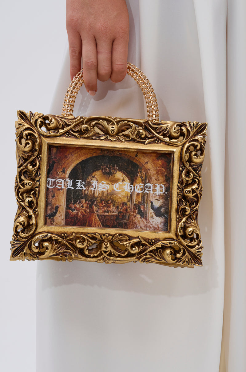 A hand holds the TALK IS CHEAP FRAME BAG, a small gold metallic handbag designed like an ornate picture frame. The center displays classic art with "TALK IS CHEAP" printed in white across the artwork.