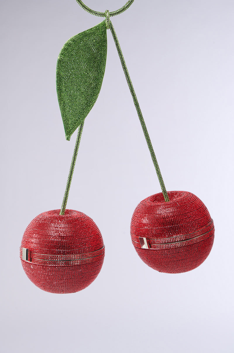 The POP MY CHERRY PURSE is a novelty piece designed as two red cherries with a green leaf and stems. Each spherical cherry has its own zipper, and rhinestone embellishments add sparkling texture to the design. 3