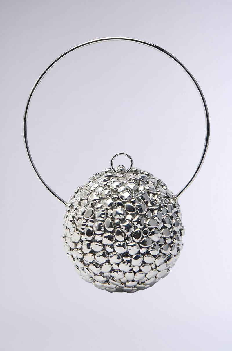 The TO THE FUTURE METAL PURSE is a metallic spherical handbag with a textured surface, featuring numerous small, shiny protrusions. It includes a large circular handle on top for crossbody wear, set against a plain white background. This accessory makes a striking statement.