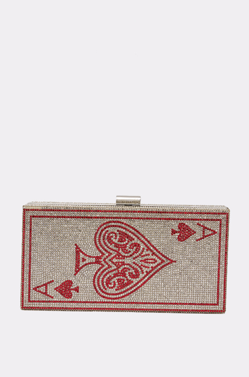 The PLAY YOUR CARDS CLUTCH is a rectangular purse styled like the ace of hearts, featuring red and silver rhinestones on a light background for dazzling casino-inspired flair. 0
