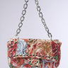 The ITS REALLY SWEET PURSE is a sweet shoulder bag flaunting a colorful floral tapestry and adorned with metal studs. It offers easy carrying with a chunky silver chain strap, set against a plain light gray background.