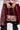 The person holds the ITS REALLY SWEET PURSE with a metal chain strap, highlighting its rose print design. They flaunt a shiny, red vinyl-like skirt and black studded pants, while a hint of white fabric from their top peeks into view.