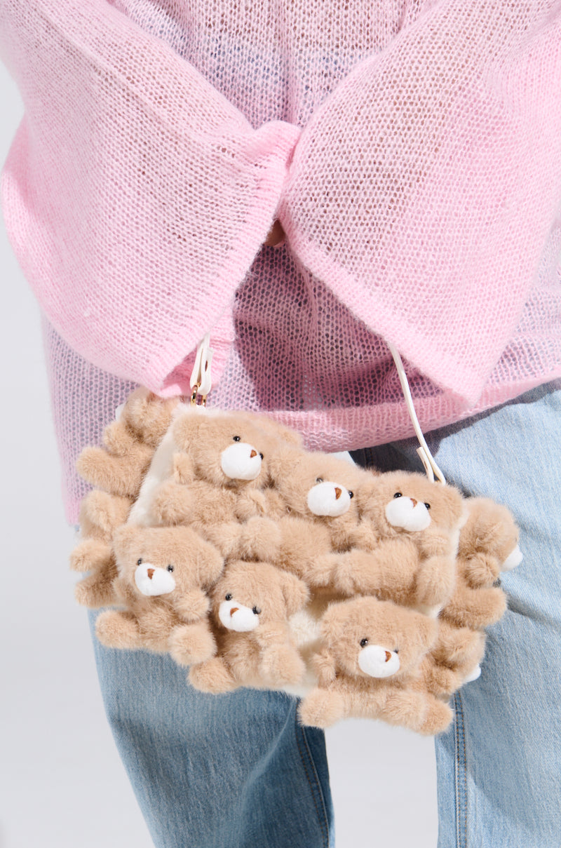 A person in a pink sweater and blue jeans holds a BEAR WITH ME PURSE made of small plush bear appliques with white faces and brown bodies, highlighting the bag's whimsical, playful design.