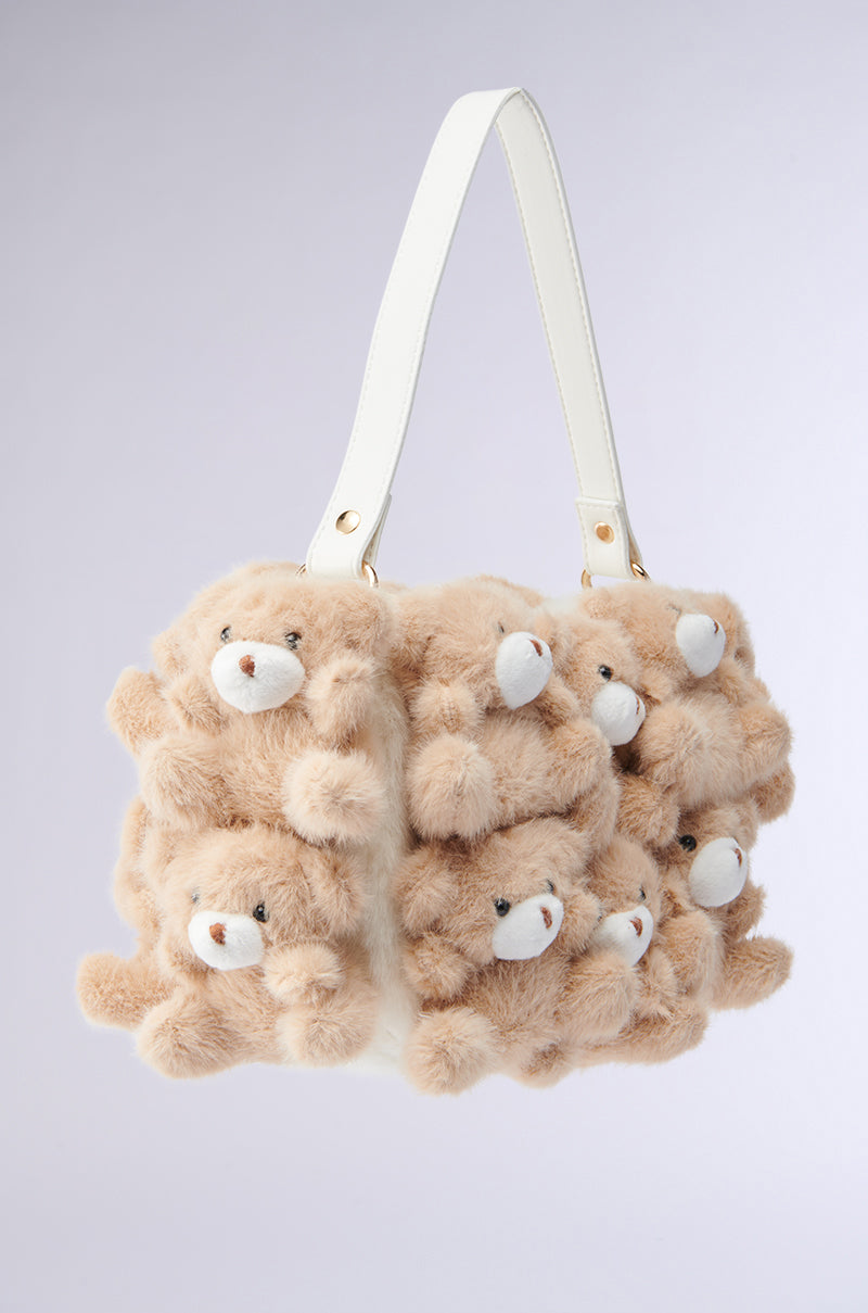 The BEAR WITH ME PURSE, a faux fur handbag with plush bear appliques featuring beige fur and white snouts, is elegantly accented by a sleek white handle, standing out against a simple light gray background.