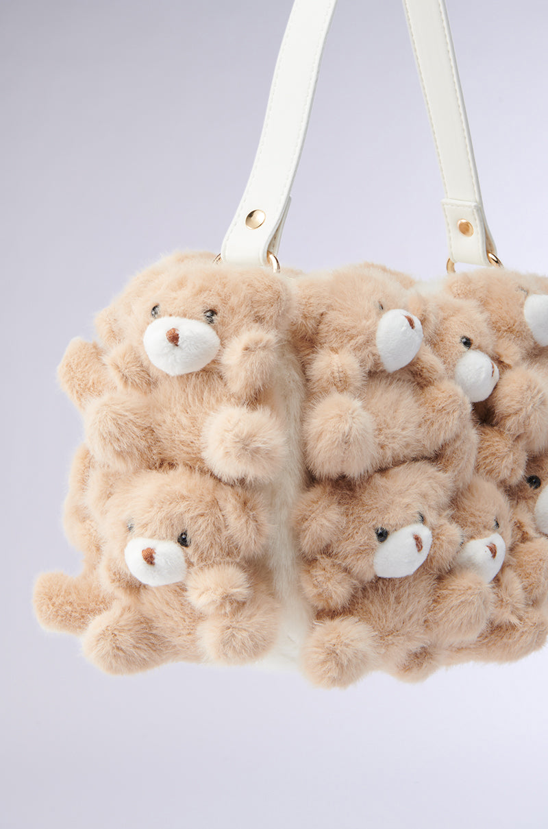 Introducing the BEAR WITH ME PURSE: a faux fur handbag decorated with plush teddy bear appliques featuring charming beige bears with white snouts and button eyes, playfully hanging from elegant white handles on a soft gray backdrop.