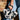 A person in blue denim holds the BUT THIS AIN'T THE FARM MINI PURSE—cow-print with black spikes and a black handle—in front of a brick wall, making a bold statement.