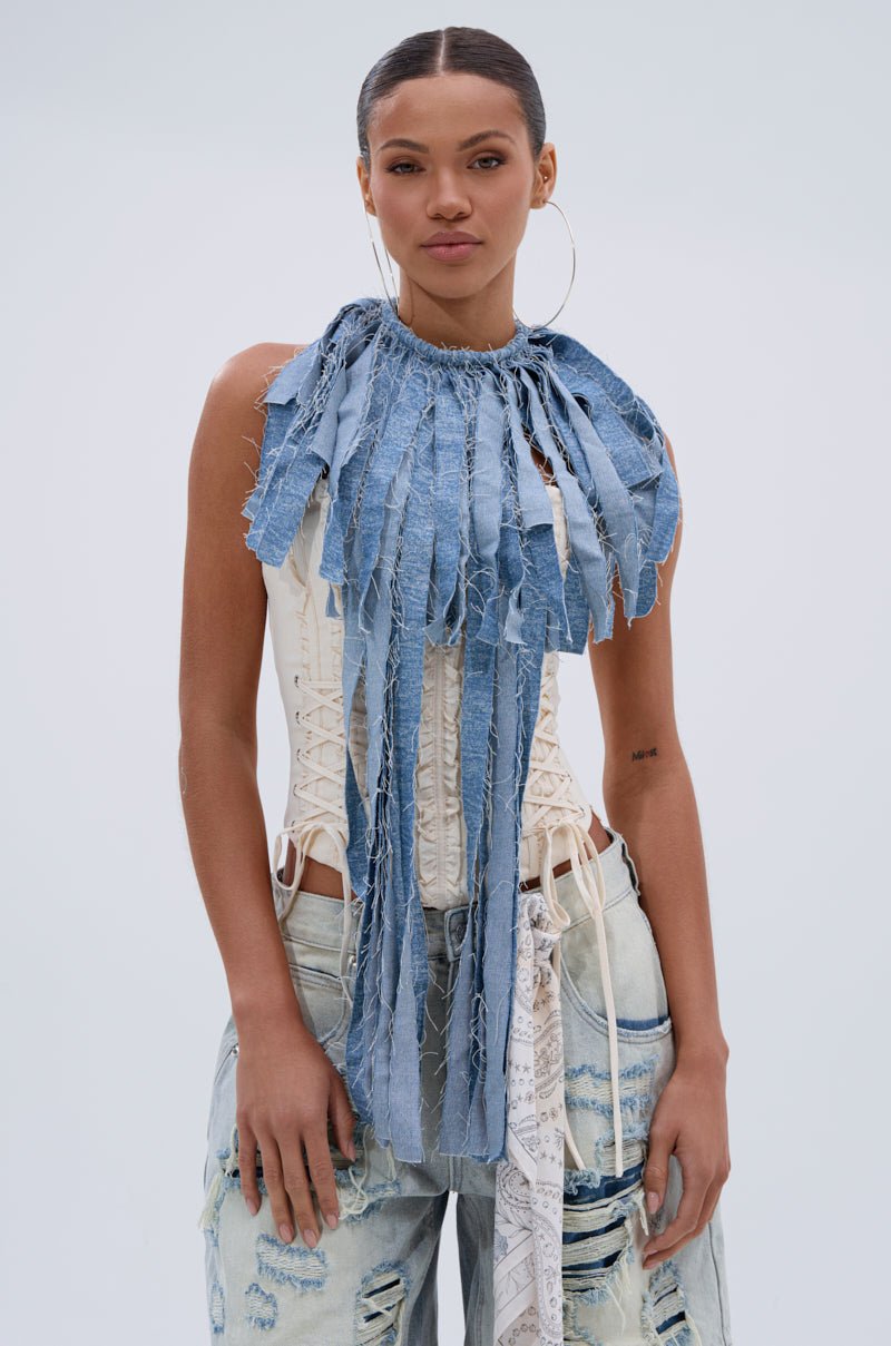 A woman wearing a sleeveless white lace-up corset top, light blue distressed jeans, hoop earrings, and the DENIM BLUE FRINGE NECKLACE stands against a plain light background.