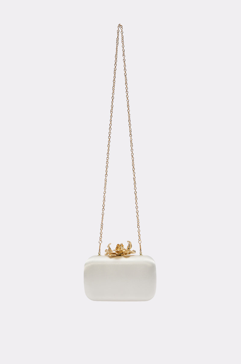 The IN ROME CLUTCH is a small, rectangular white satin bag with gold-tone hardware, a chain strap, and a decorative gold clasp, displayed against a plain light background.