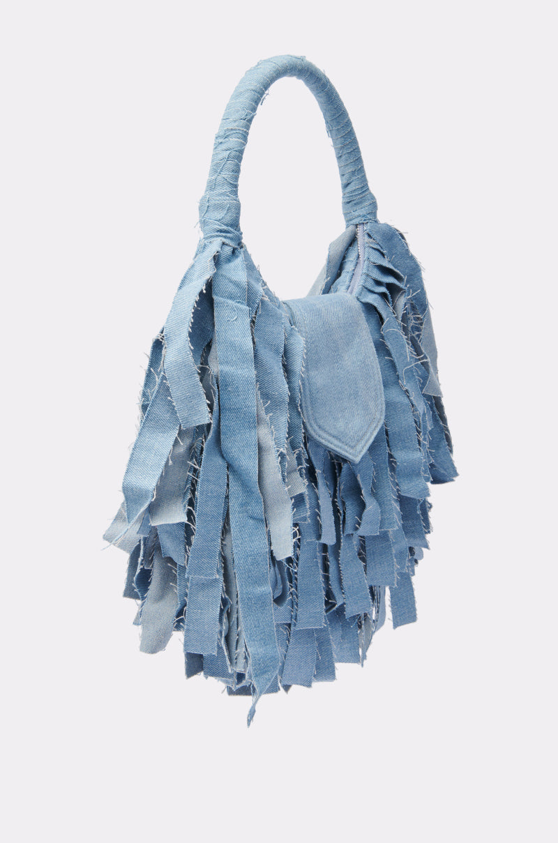 The SUZIE DENIM FRINGE PURSE is a light blue denim handbag with a rounded handle and layered, frayed strips for a textured, fringed look that’s casual and unique.