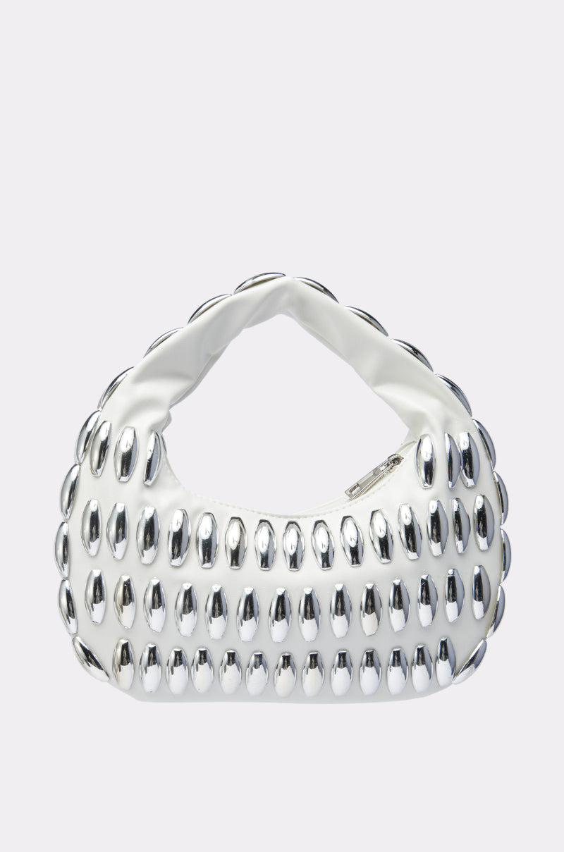 The IT GIRL PURSE is a chic white faux leather handbag with a baguette silhouette, rounded handle, and oval silver studs arranged in rows, shown against a plain light background.