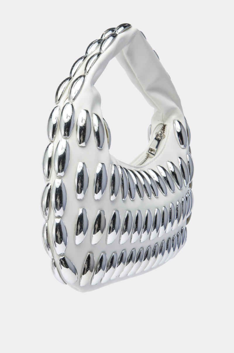 A chic accessory, the IT GIRL PURSE is a white handbag with a padded handle and rows of shiny, oval silver embellishments, shown against a plain light background.