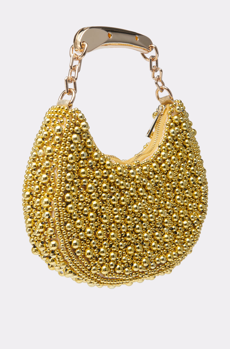 The POP CHAMPS PURSE, a small crescent-shaped bag with gold metallic beads, gold metal handle, and zipper, shines against a plain light background—a stunning statement accessory.