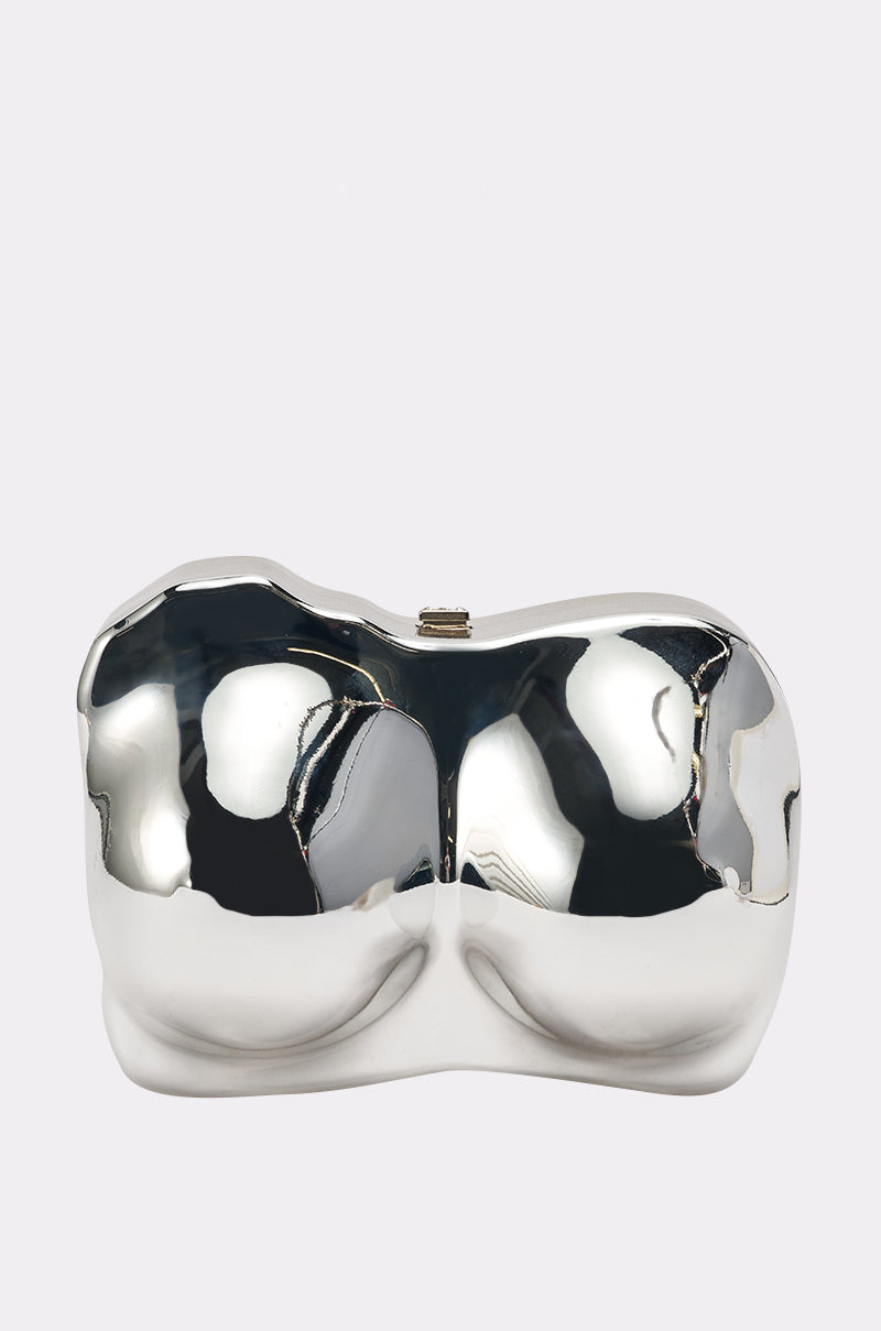 The A BIT BUSTY CLUTCH is a shiny, metallic silver bag shaped like a stylized human torso and hips, with smooth, reflective curves, displayed against a plain light background.