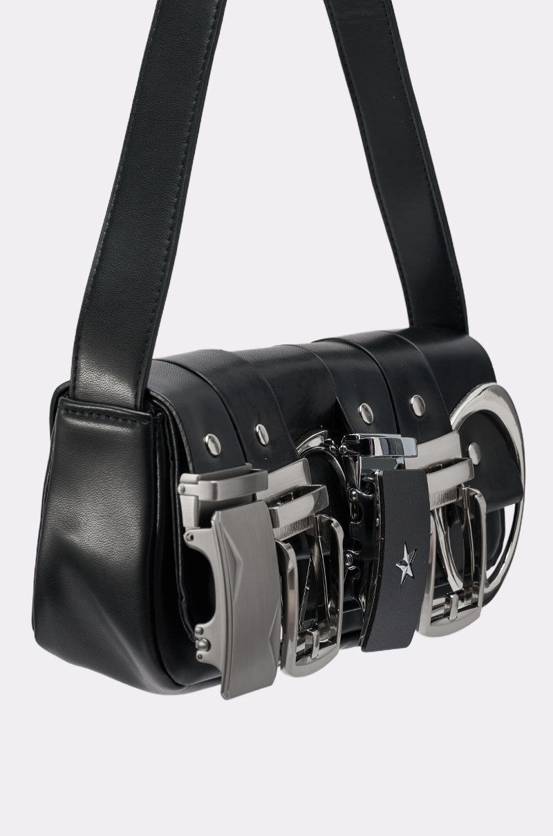 The BUCKLE UP PURSE is a black vegan leather bag with a wide strap, detailed with multiple oversized metallic belt buckles as closures on the front.
