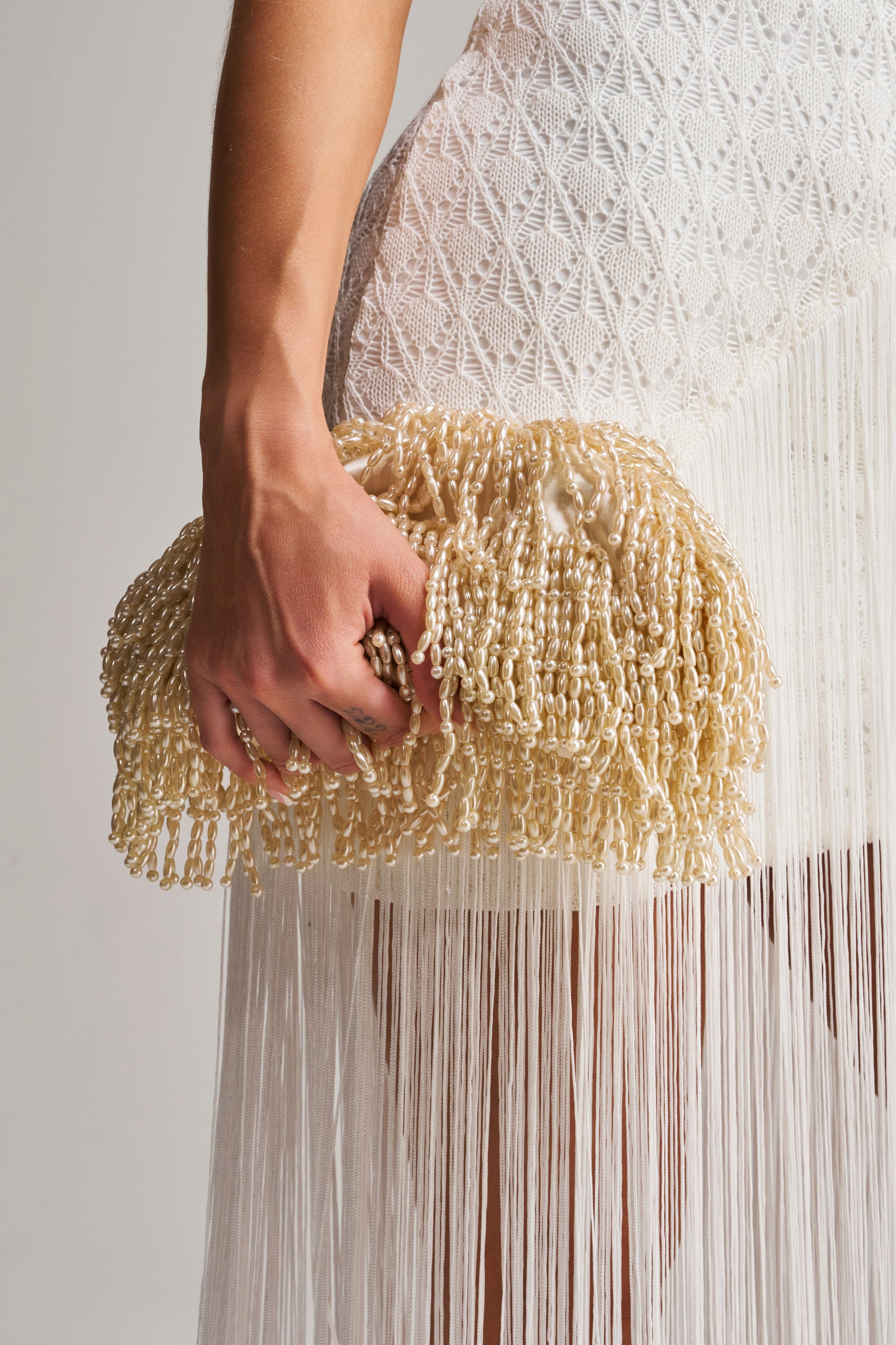 A person pairs a white fringed dress with the ON AN ISLAND PEARL CLUTCH, combining intricate patterns and textured pearl details for an elegant, stylish look.