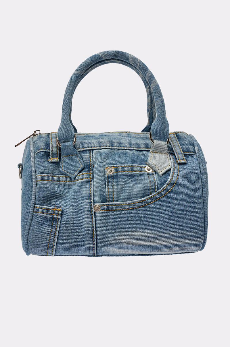 The NO BLUES DENIM PURSE is a mini denim bag styled like jeans, with jean-like pockets, seams, blue denim handles, and a zip closure. Photographed against a plain light background. 0