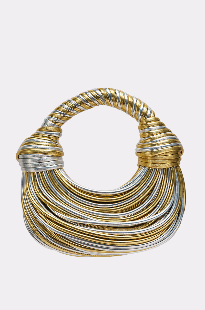 The FIND ME OUTSIDE PURSE is a sculptural crescent bag with gold and silver wrapped metallic bands, a twisted handle, and a rounded layered design set against a plain light background. 1