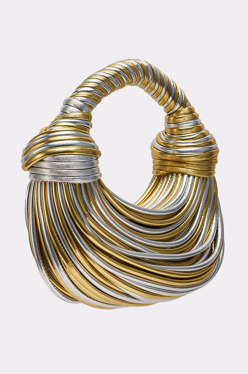 The FIND ME OUTSIDE PURSE features intertwined gold and silver metallic bands forming a sculptural, rounded shape with a twisted handle, displayed against a plain light gray background. 3