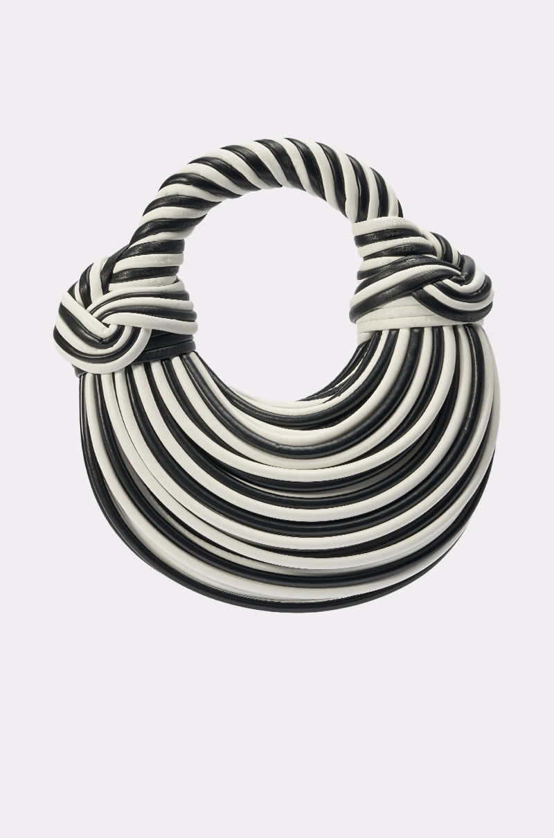 The COULDN'T DECIDE PURSE, a round black and white faux leather bag with a braided handle and alternating curved bands for a striped pattern, sits against a plain light background. 0