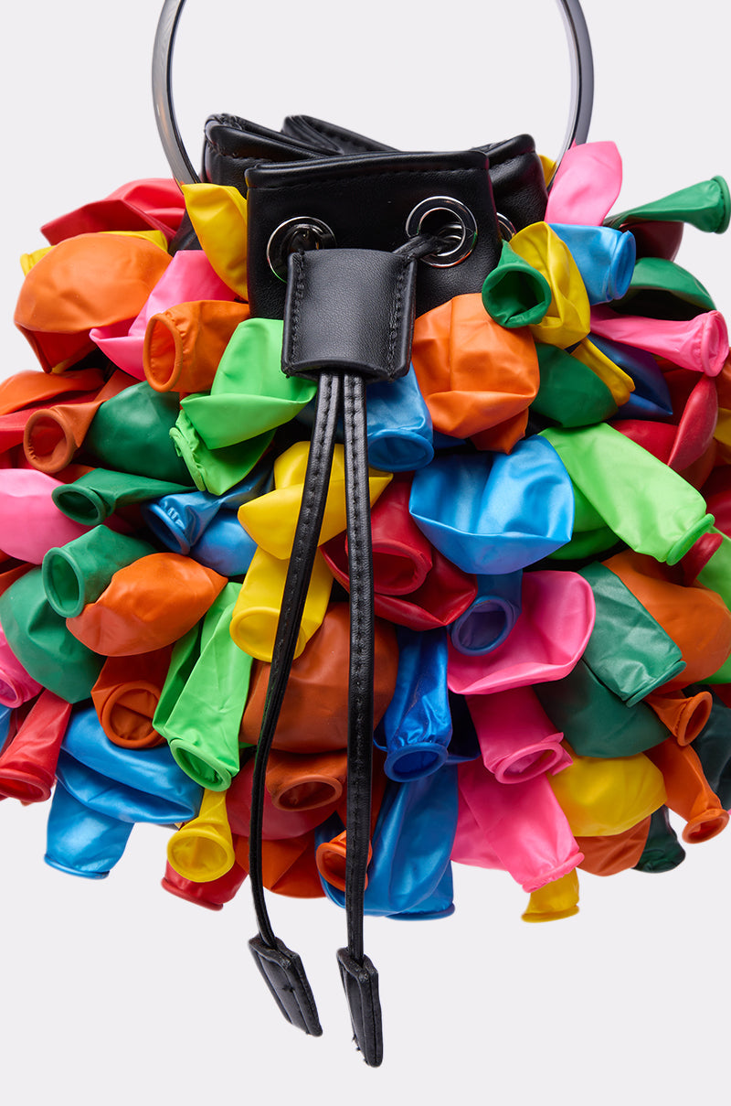 The BLOW ME BUCKET BAG is a black faux leather handbag featuring clusters of colorful, deflated balloons all over its surface for playful balloon detailing and a vibrant texture. 3