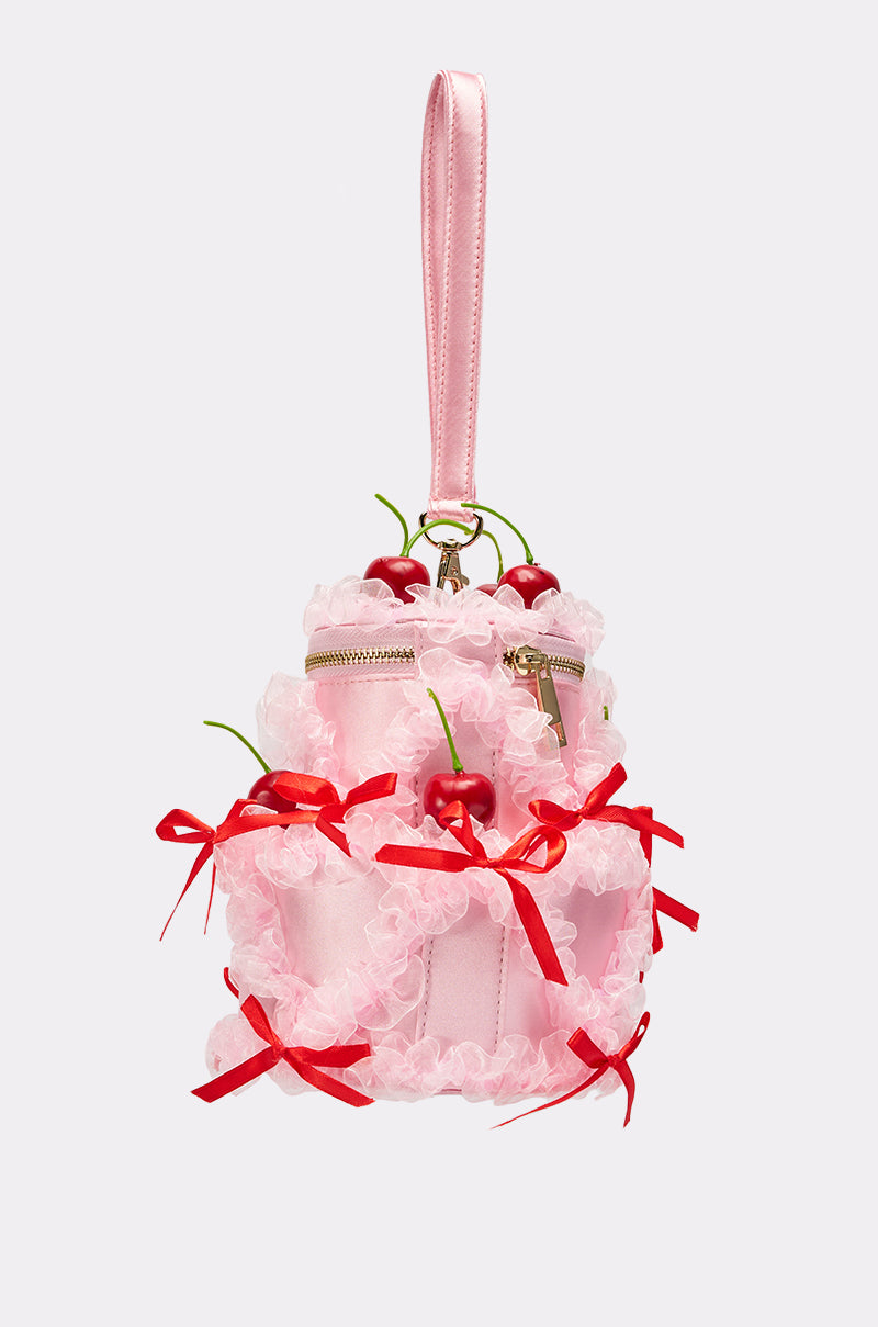 The MARIE CHERRY PURSE is a pink satin bag with sheer ruffles, red bows, cherry accents, a shiny wrist strap, zipper closure, and topped with playful artificial cherries.