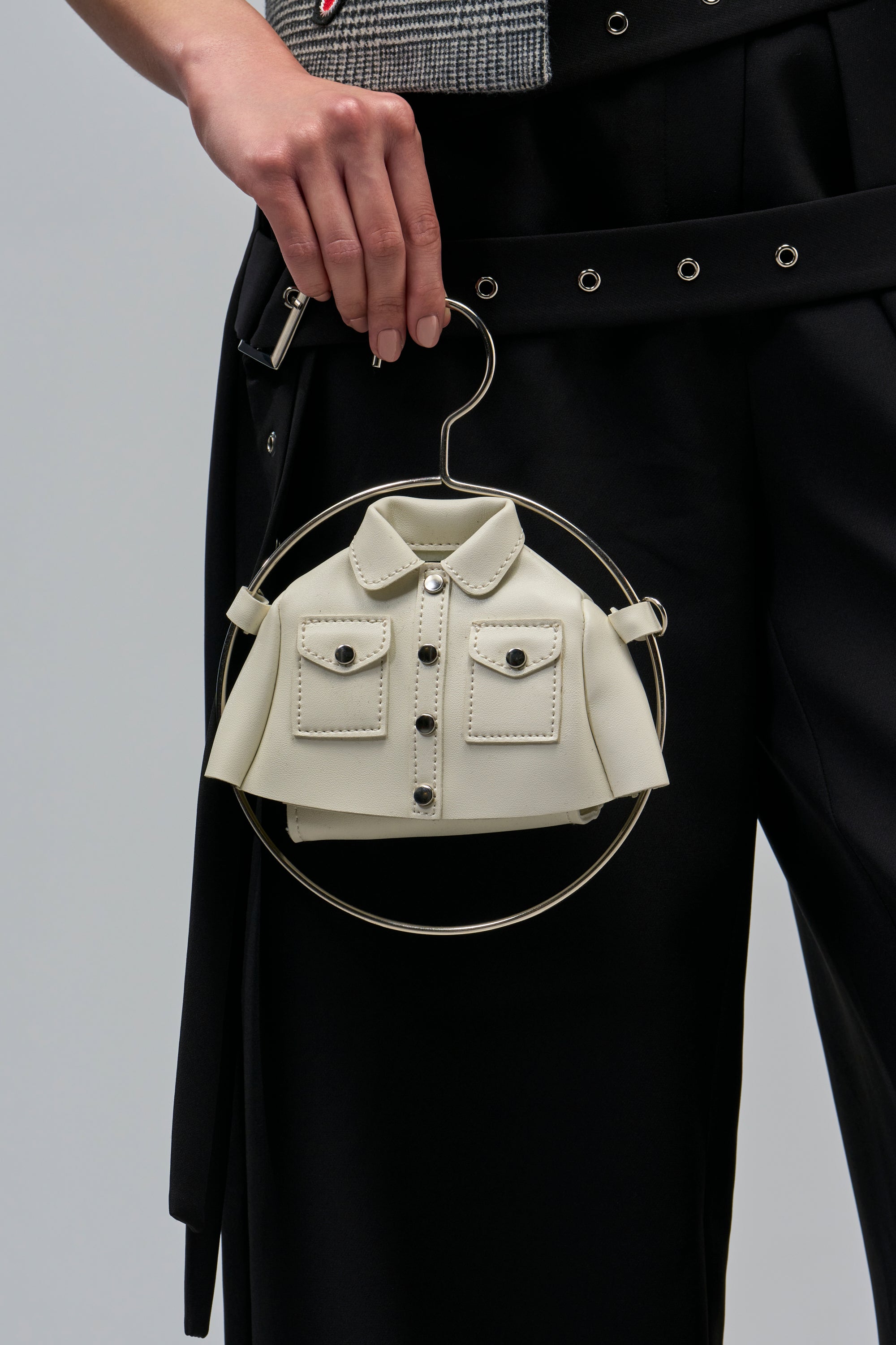 A hand holds a white WHERES MY JACKET MINI PURSE, designed like a miniature jacket hanging from a circular metal handle.
