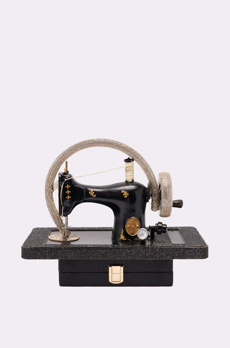 The SEW CUTE PURSE, a vintage sewing machine-shaped bag with gold and rhinestone accents, rests on a textured rectangular base against a plain white background. 0