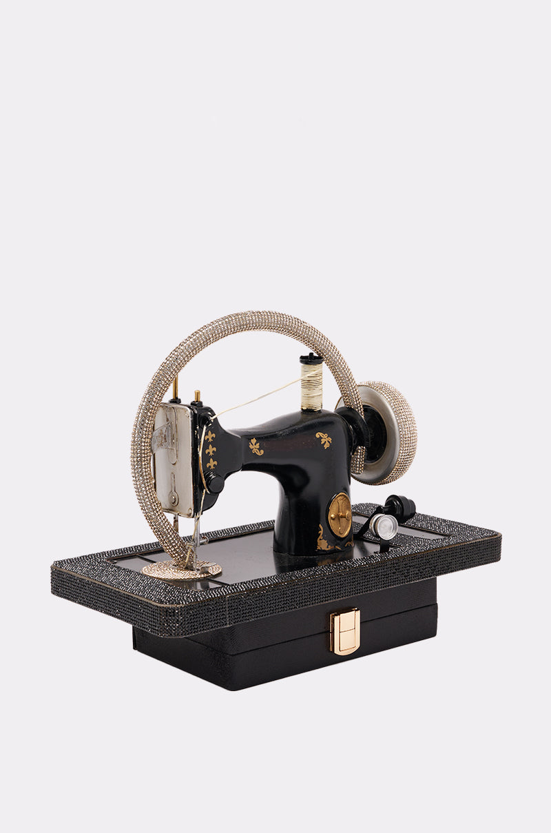 The SEW CUTE PURSE is a vintage-inspired black sewing machine-shaped handbag with rhinestone accents, a textured rectangular base, and a gold clasp, shown against a plain white background. 2