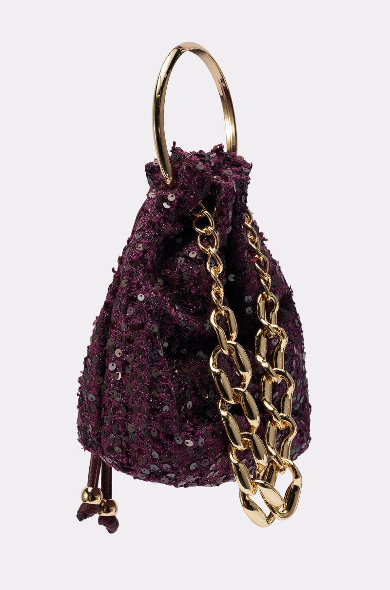 The KARY TWEED BUCKET BAG is a small, dark purple sequined mini bucket bag featuring a gold-tone handle ring and chunky gold chain, shown against a plain light background.