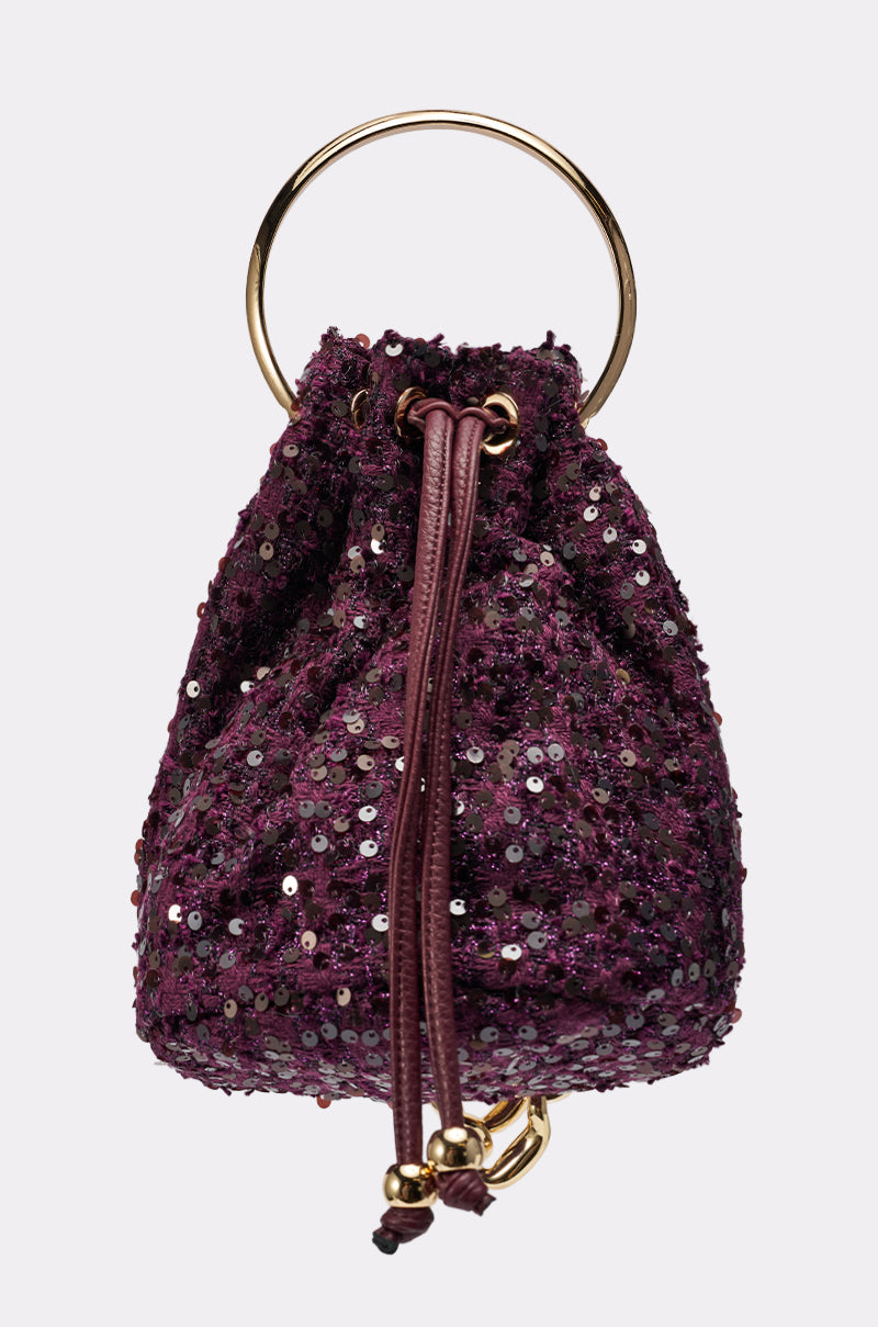 The KARY TWEED BUCKET BAG is a small bucket bag with purple sequins, gold metal handle, and gold accents, displayed against a plain light background.