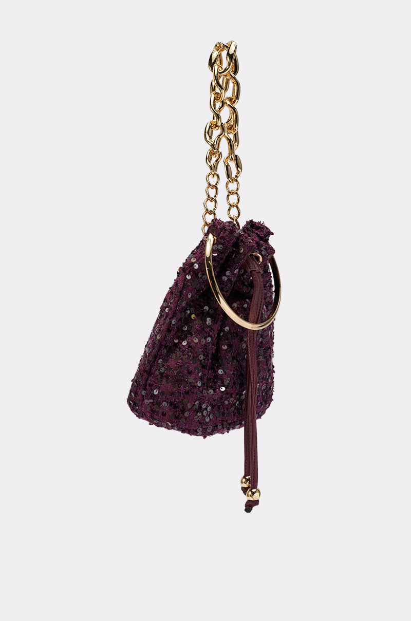 The KARY TWEED BUCKET BAG is a small, purple sequined mini bucket bag featuring a gold-tone chain handle and circular gold ring detail, displayed against a plain white background.