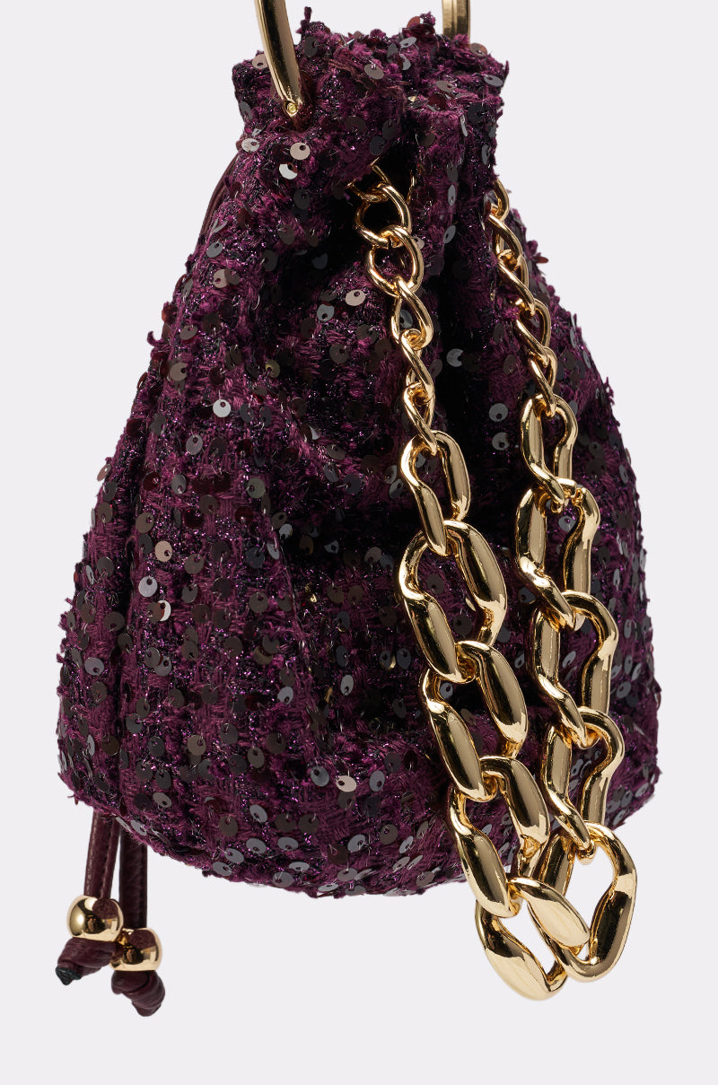 The KARY TWEED BUCKET BAG is a small, deep purple sequined mini bucket bag featuring a chunky gold-tone handle and gold hardware, photographed against a plain light background.