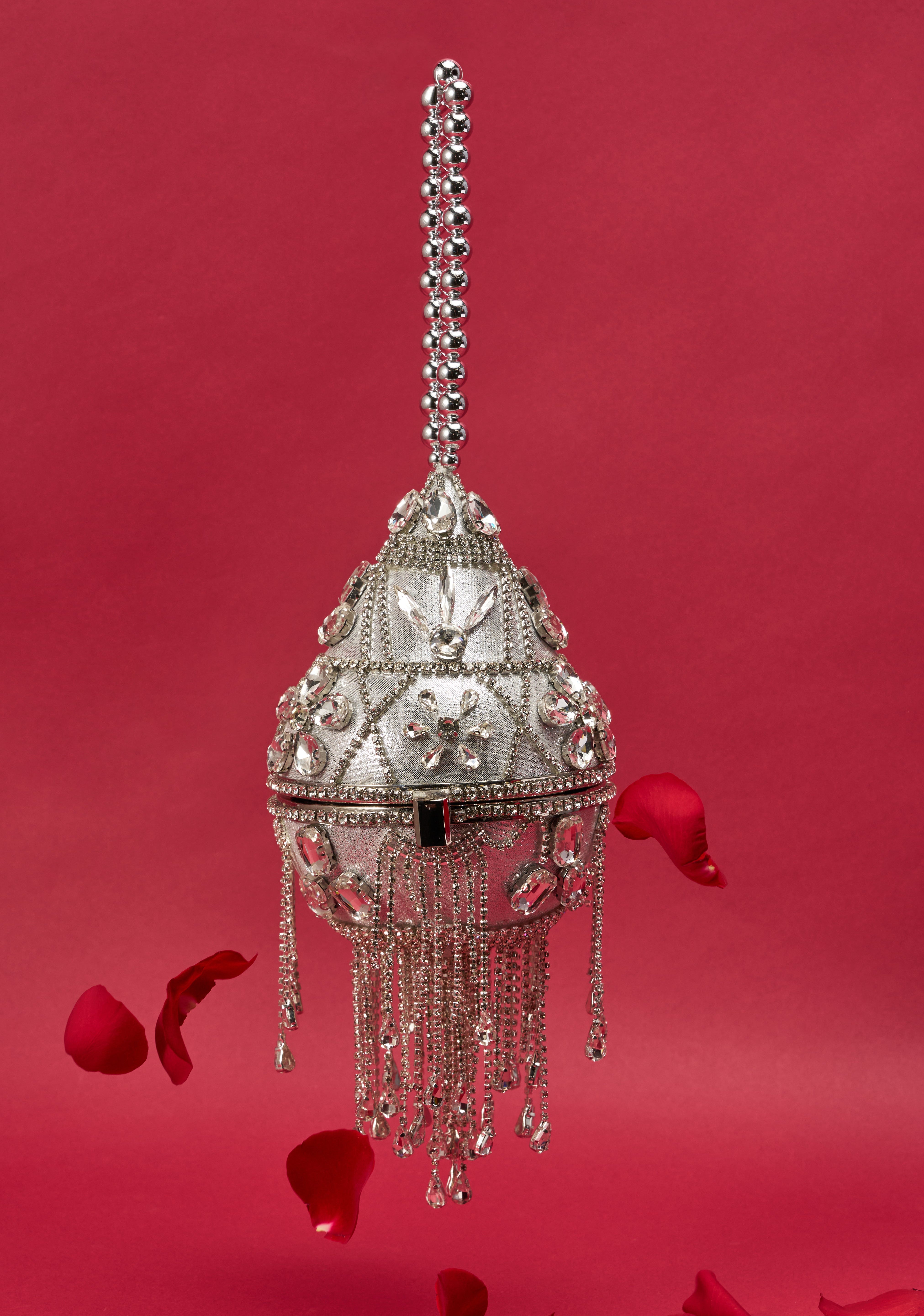 The DECO BLING BAG—a silver, bejeweled crystal fringe purse with a decorative handle—hangs against a red backdrop, rose petals scattered below, making it the ultimate statement accessory. 3