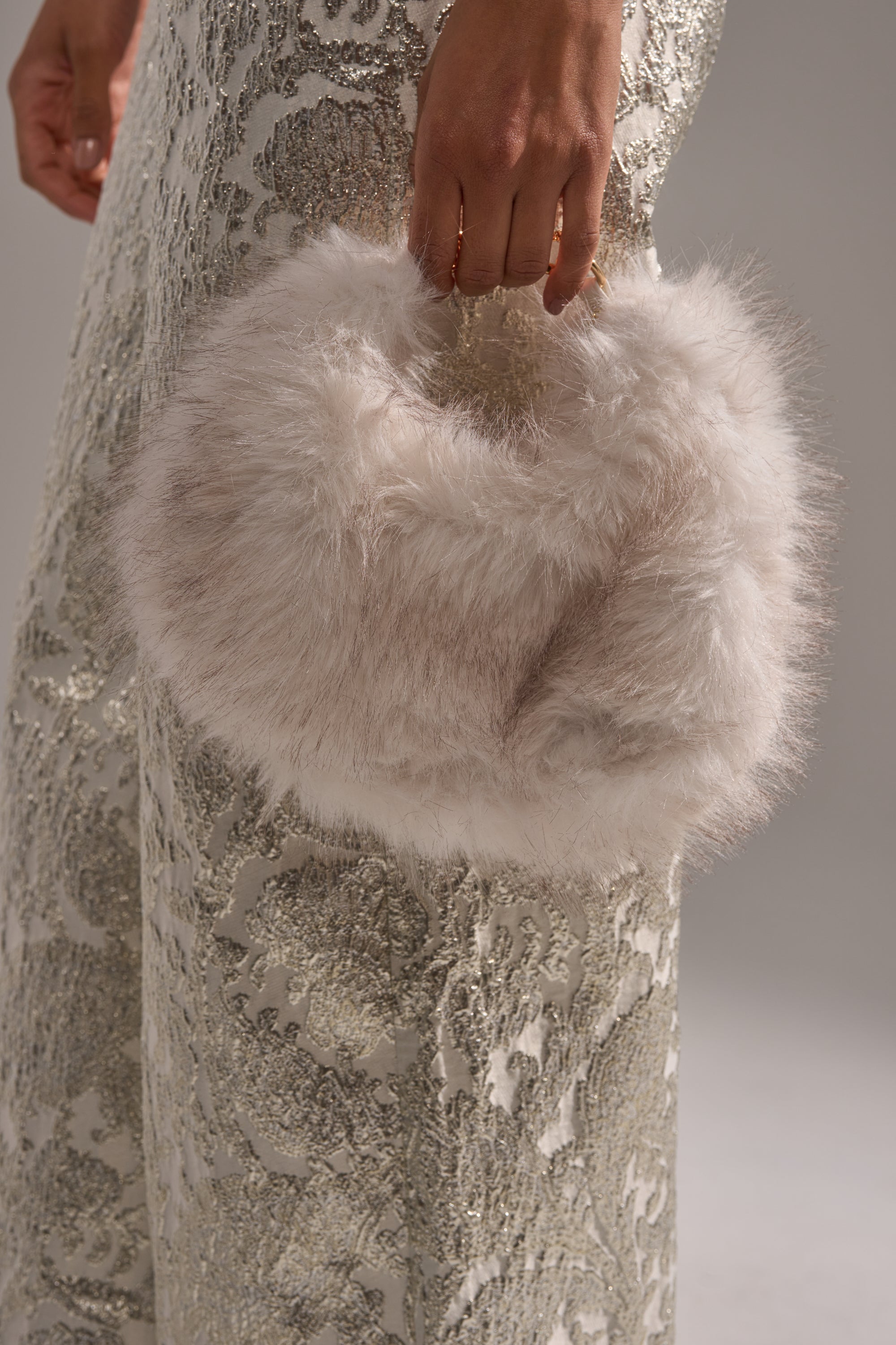 A person in a sparkly, silver-patterned dress holds the WINTER SKY FAUX FUR PURSE by its handle, their hand resting gently on the plush faux fur. 1