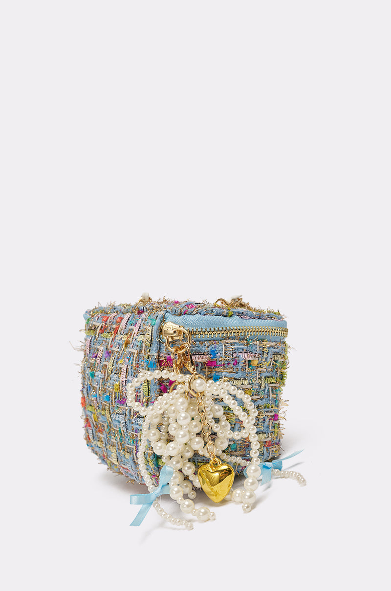 The I HAVE CLASS TWEED PURSE is a pastel tweed mini crossbody bag with gold zipper accents, a gold chain strap, and a pearl charm featuring blue ribbons and a gold heart, shown against a plain white background. 2