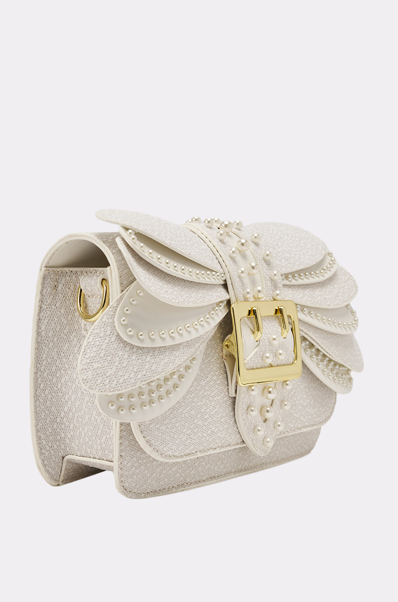 The LIKE A BUTTERFLY PURSE is a stylish cream evening bag with layered petal-like flaps, adorned with small pearls and a bold gold buckle on the front, showcased against a plain white background. 2