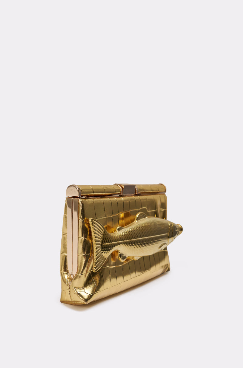 The GONE FISHIN CLUTCH is a gold croc-embossed purse with a textured pattern and a large fish ornament. It features a removable crossbody chain for versatile styling, shown against a plain light background. 5