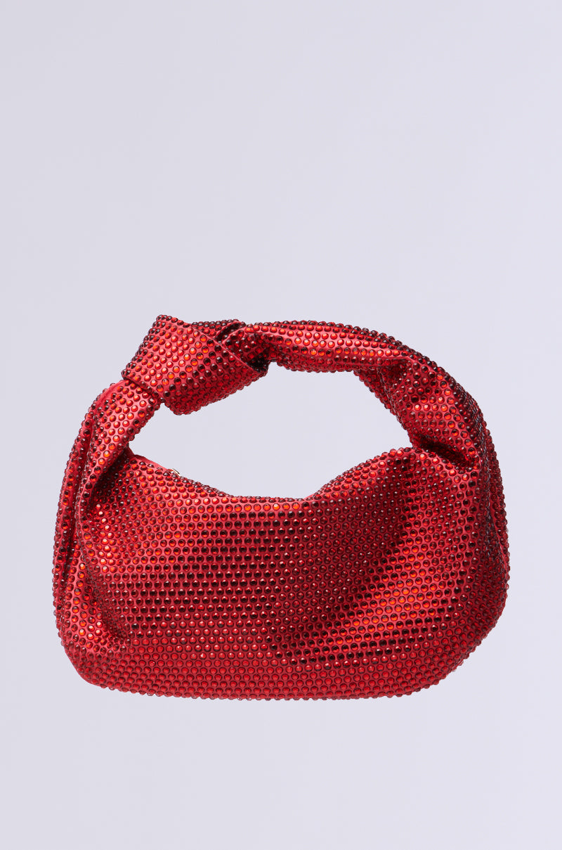 The GLITZ AND GLAM BLING PURSE is a chic red textured handbag with a knotted handle, adorned with sparkling rhinestones on a plain gray background—ideal for carrying night-out essentials stylishly and elegantly.