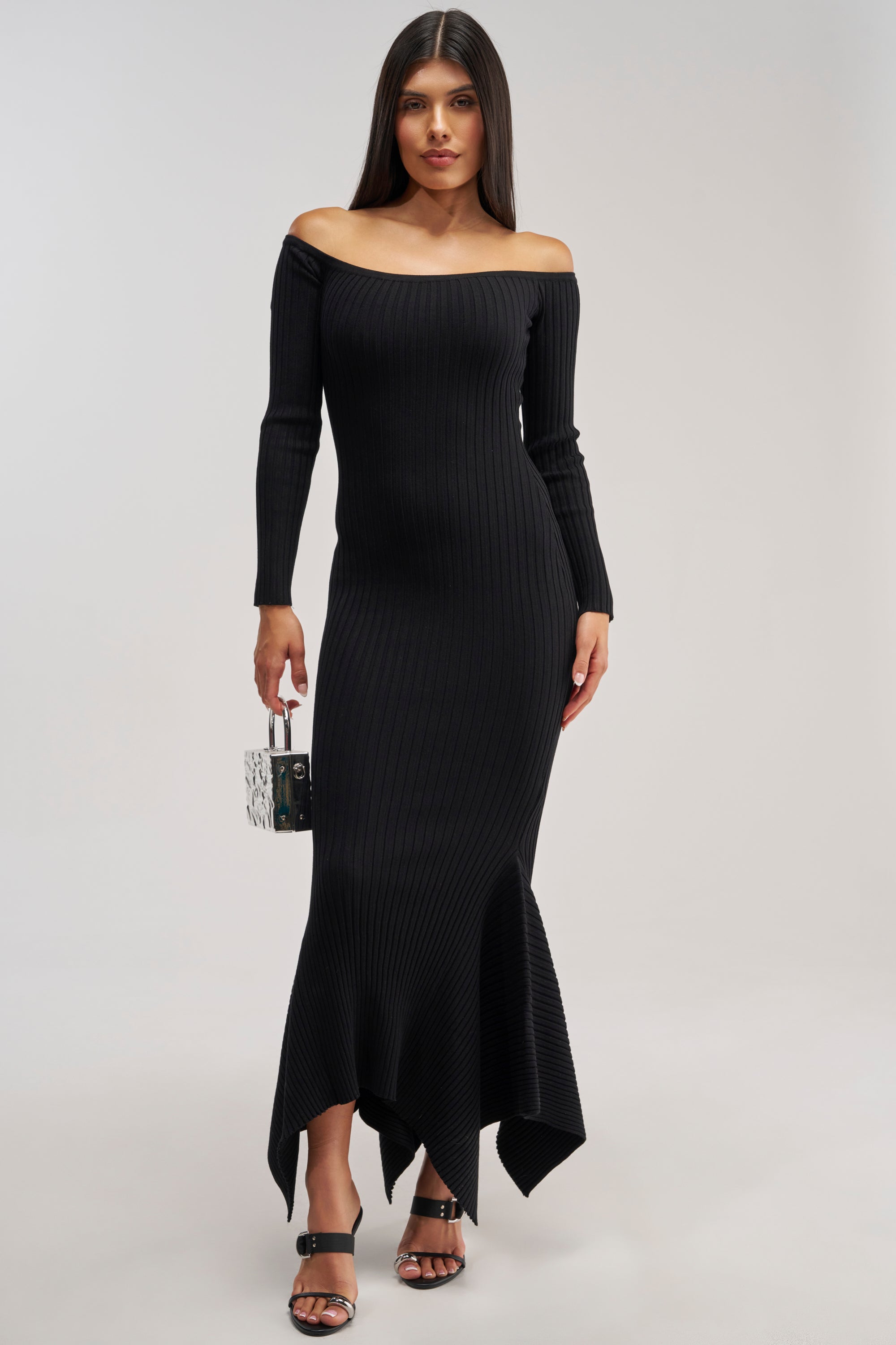 Wearing the SO SWEET KNIT MAXI DRESS IN BLACK— a long, off-the-shoulder sweater dress with ribbed detailing and an asymmetrical hem— she pairs it with a small handbag and black heeled sandals. This effortlessly chic look makes for the perfect winter date night dress.