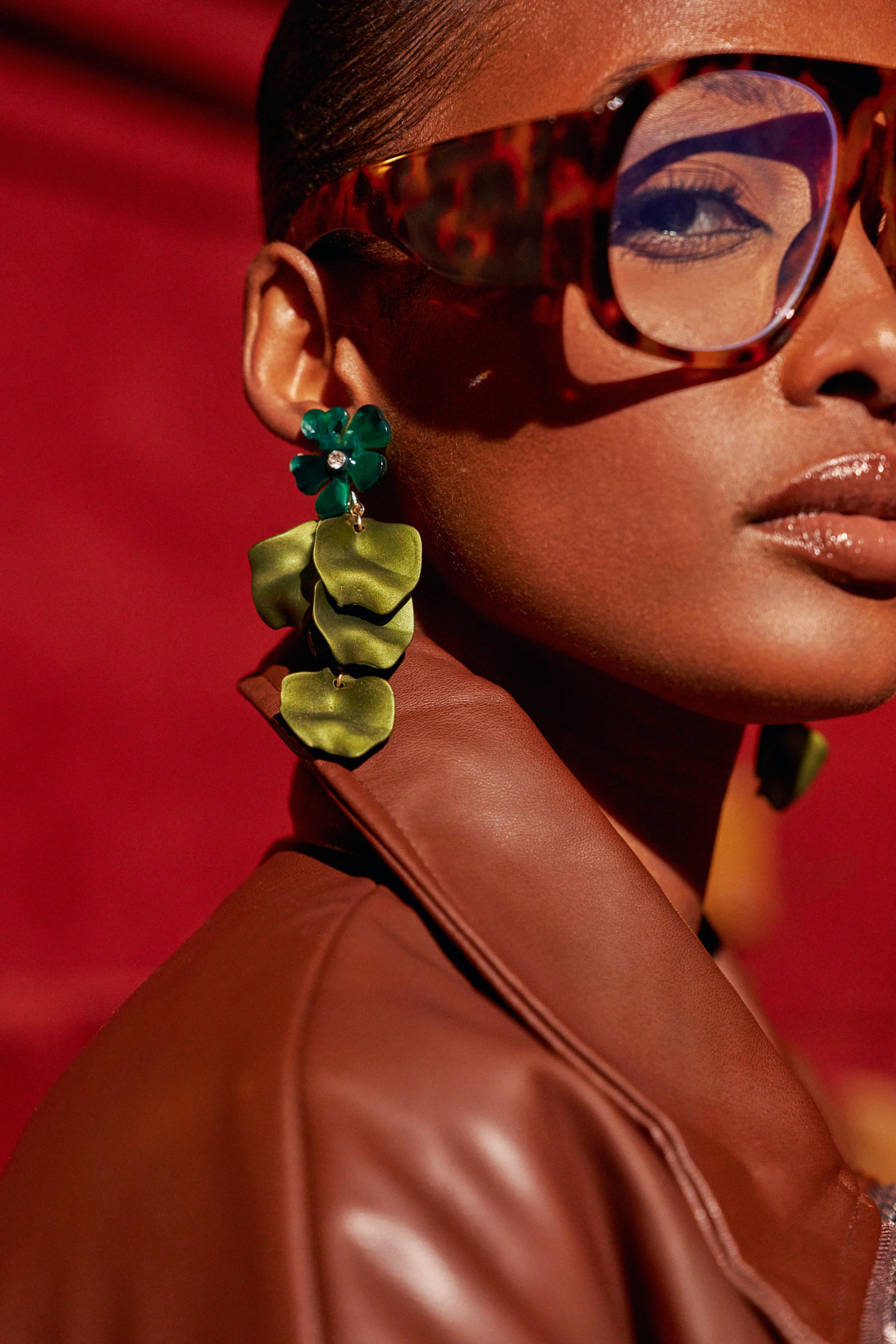 A person wearing FOREST BABE DANGLE EARRING, featuring a dark green floral stud and three cascading, layered green leaf-shaped charms.