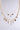 The CHARMED LIFE GOLD NECKLACE is a two-layered piece with gold charms—crosses, hearts, locks, a key, and a rose. Shiny jeweled accents make it an elegant statement for any outfit.