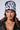 A woman with long brown hair is wearing the ALL WE NEED IS MONEY BEANIE, a black stretch knit hat featuring contrast text lettering. She completes her edgy look with a black leather jacket and a silver chain necklace, all set against a neutral background.