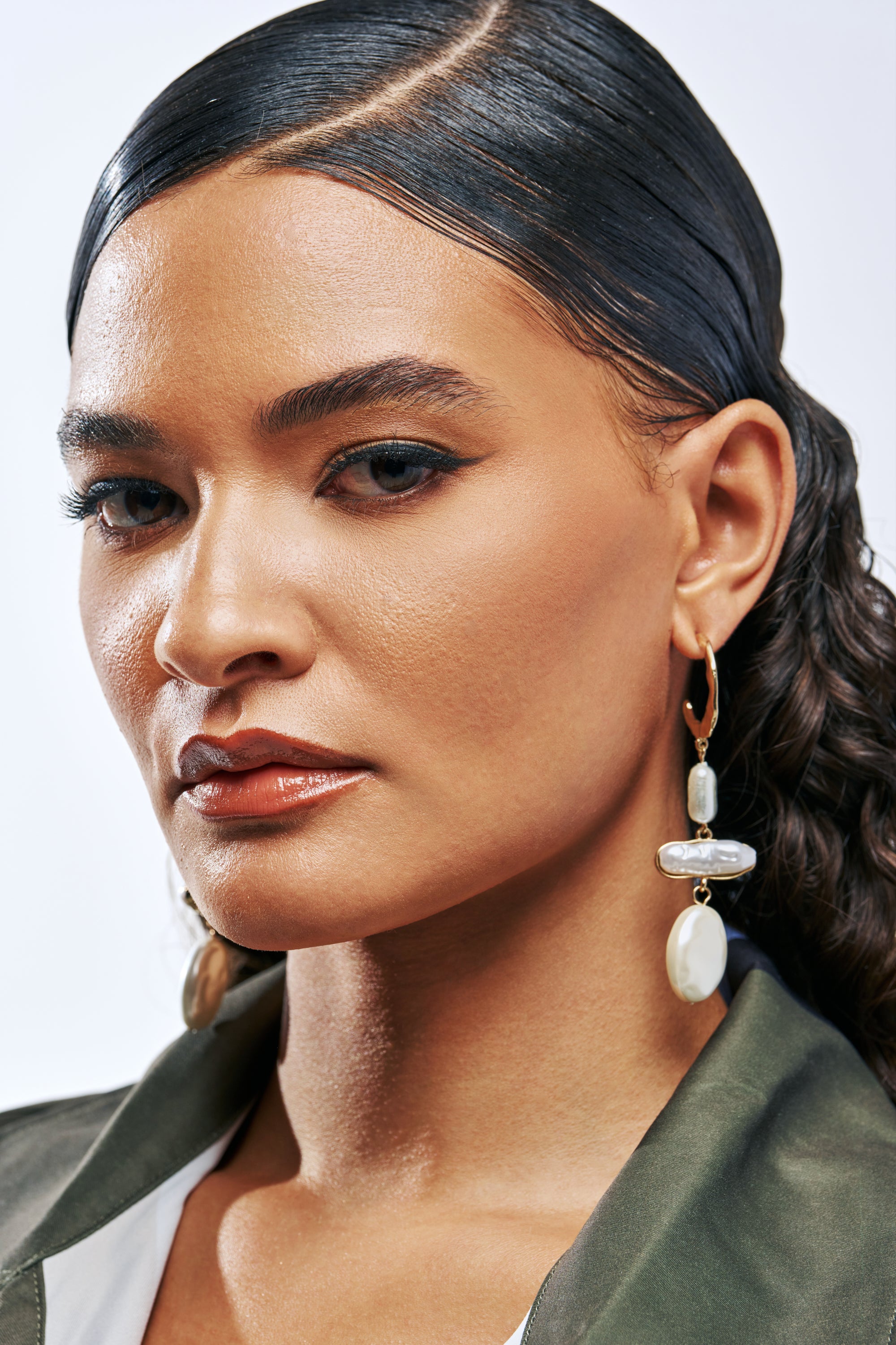 Close-up of a woman wearing TRIPLE LAYER PEARL EARRINGS, featuring gold hammered hoop earrings with three dangling, irregular-shaped white pearls.
